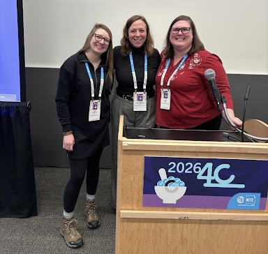 Three women stand together at a podium, smiling, in a conference setting.